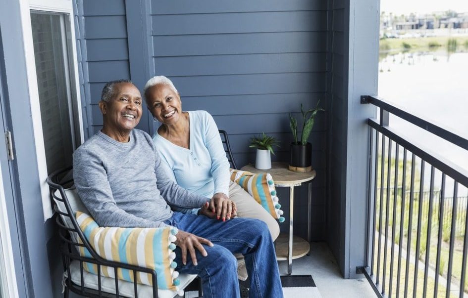 Home care - An elderly couple peacefully seated on a balcony, pondering the decision of aging in place versus moving to a retirement home.