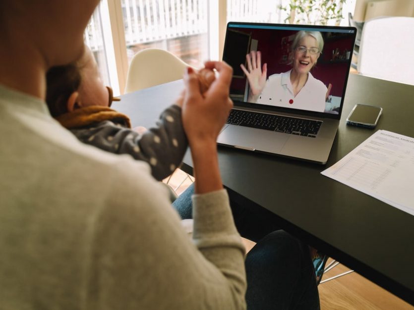 A woman and child sit at a table with a laptop, engaged in long distance caregiving for aging in place.
