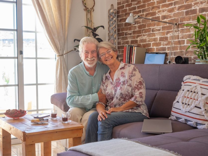 Continuing to Live at Home for Seniors, enjoying each other's company on a couch, with a view of the outside through a window.