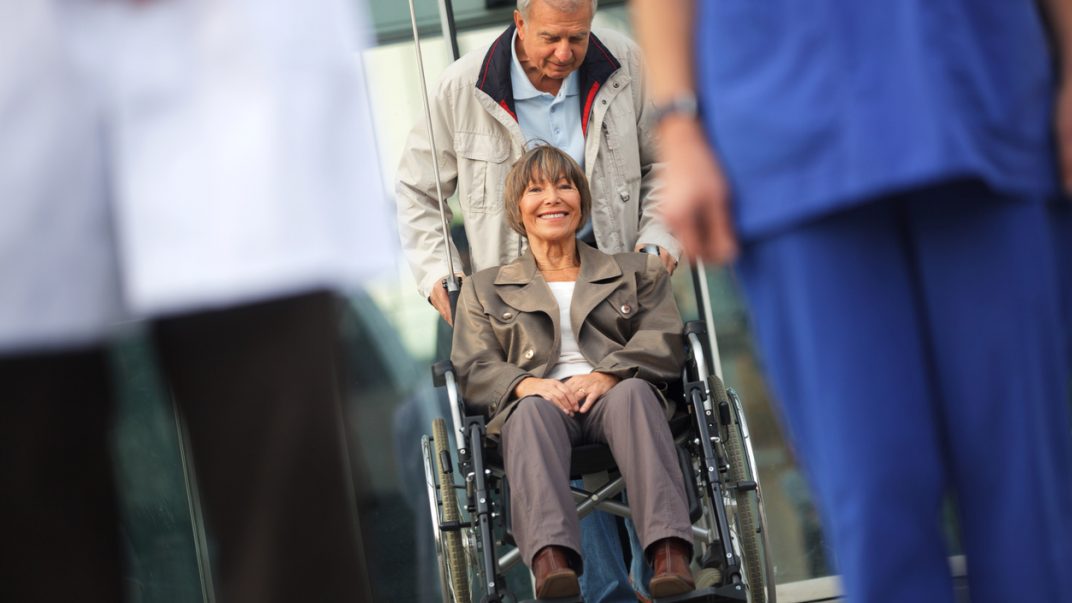 Going home: Plan your transition before being discharged 1 Older man pushing smiling older woman out of the hospital in wheelchair.