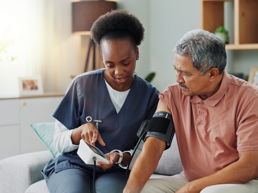 Elderly man getting blood pressure measured by a healthcare professional in his home.
