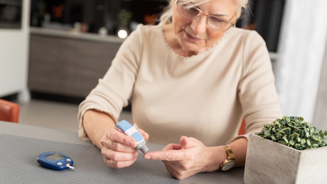 Older adult female checking her blood sugar at home using a monitoring device.