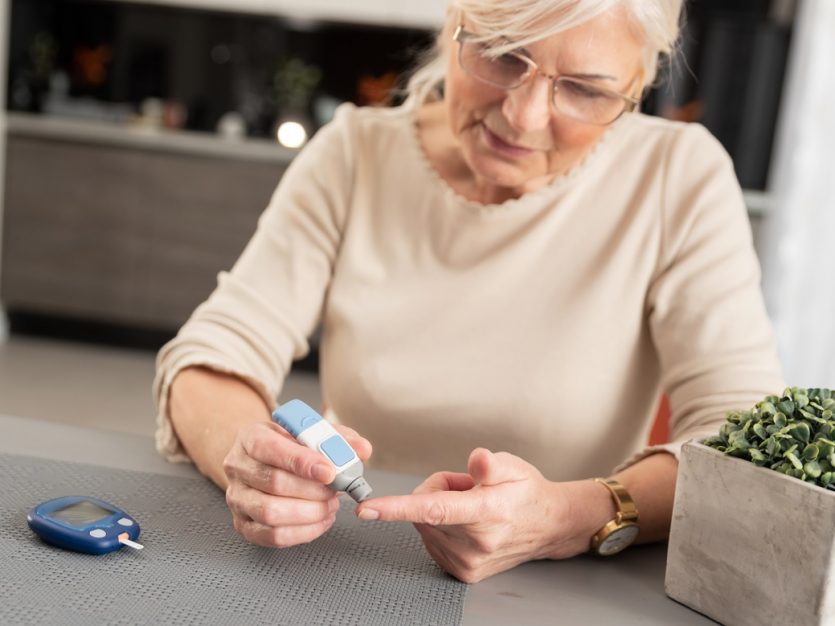 Older adult female checking her blood sugar at home using a monitoring device.