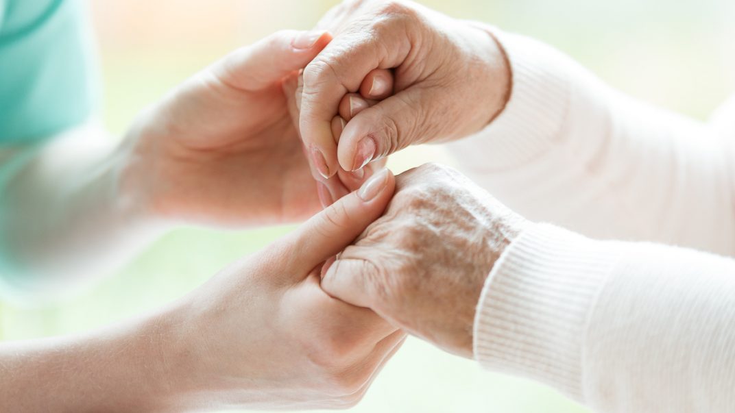 Close-up of caregiver and an elderly patient holding hands.