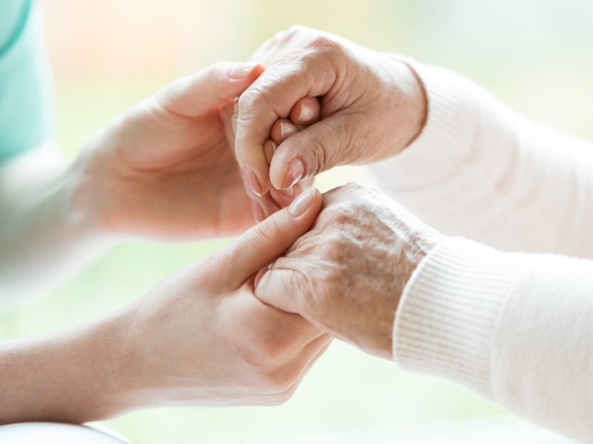 Close-up of caregiver and an elderly patient holding hands.