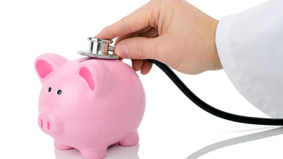 Combining health and financial well-being 1 Hand placing a doctors stethoscope on top of a pink piggybank.