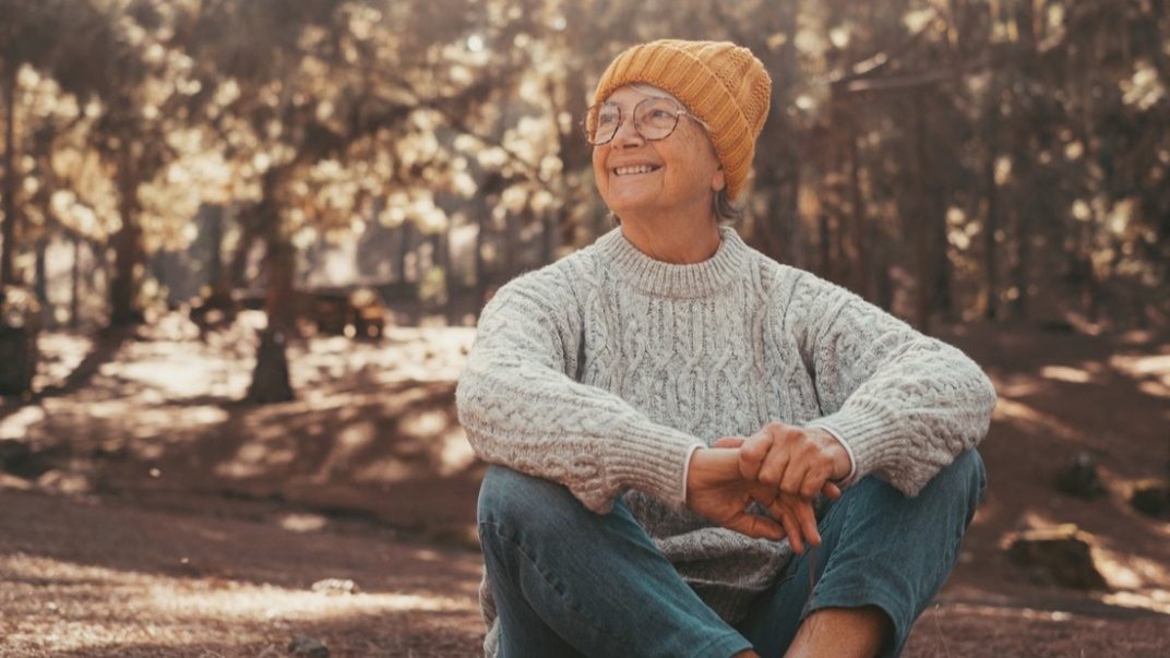 Elderly female sitting on the ground in a forest.
