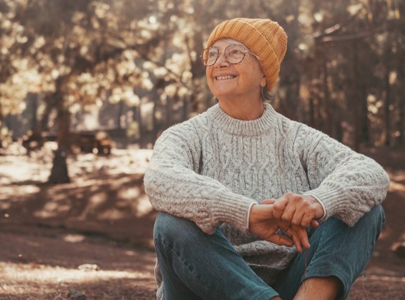 Elderly female sitting on the ground in a forest.
