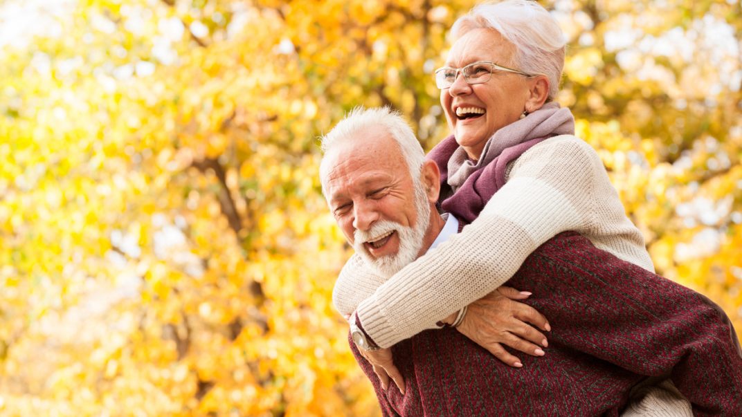 Laughing senior couple with fall coloured trees in the background.