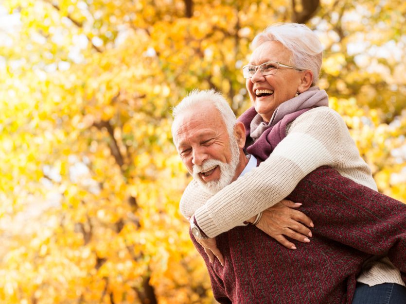 Laughing senior couple with fall coloured trees in the background.