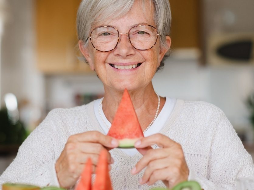 Elderly woman sitting down and smiling with a slice of watermelon in her hands.