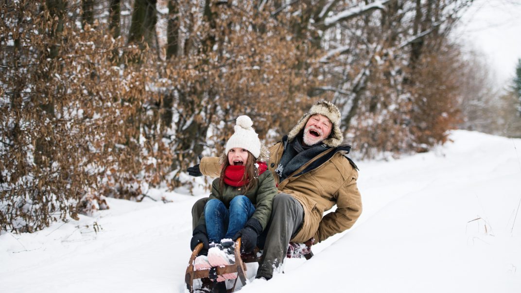 Emotional closeness between grandparents and grandchildren 1 Senior grandfather and young granddaughter sledding and smiling on a winter day.