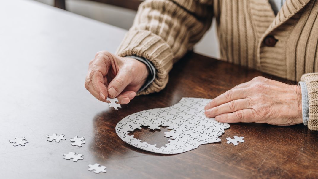 Senior man playing with a puzzle of an outlined head with missing pieces in the centre.