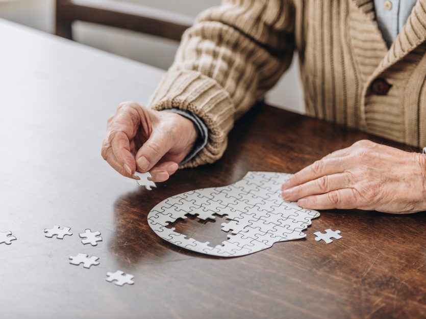 Senior man playing with a puzzle of an outlined head with missing pieces in the centre.