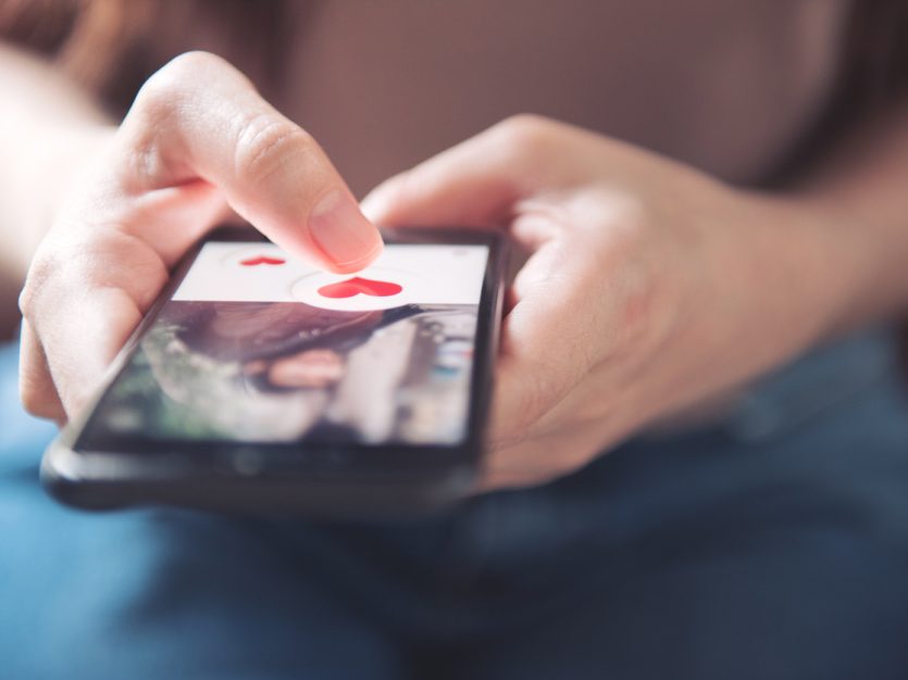 Finger of woman pressing heart icon on screen in a mobile smartphone dating app.
