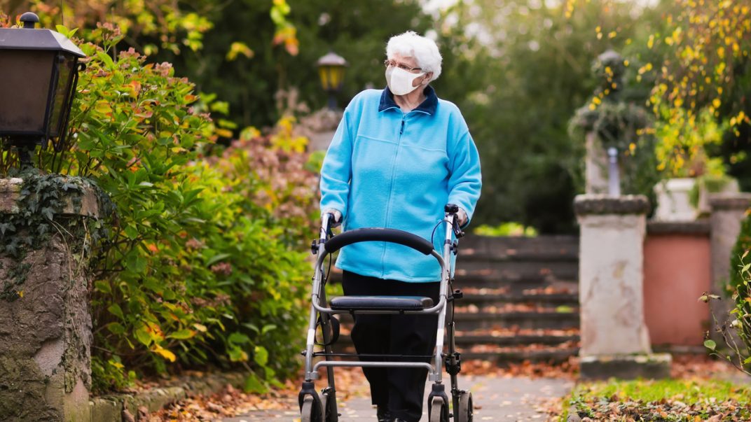 Senior woman in a surgical mask pushing walker in a park.