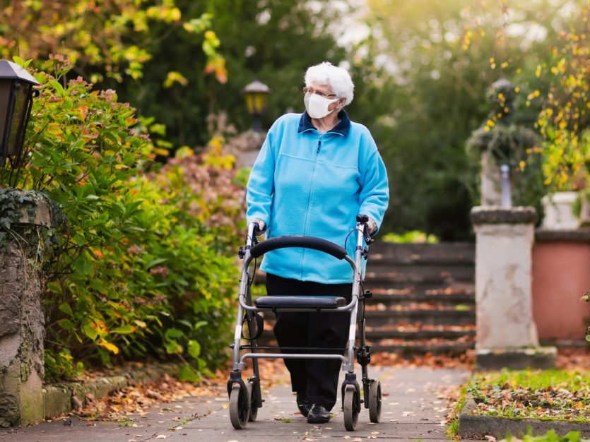 Senior woman in a surgical mask pushing walker in a park.
