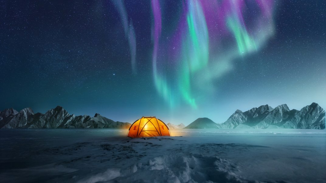 What's on your bucket list? 1 A glowing tent pitched up in the snow at night with the northern lights flickering in the sky above.