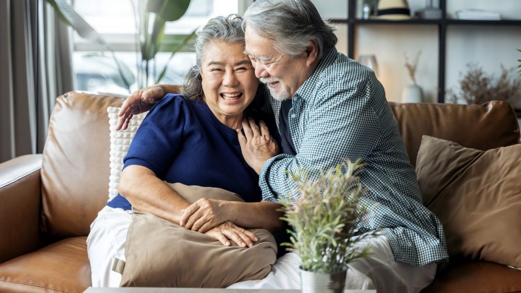 Retired couple hugging and laughing together on the sofa at home.