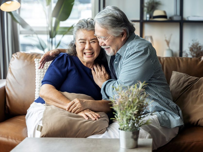 Retired couple hugging and laughing together on the sofa at home.