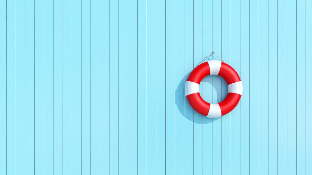 Red lifebuoy hanging up on light blue wooden planks.