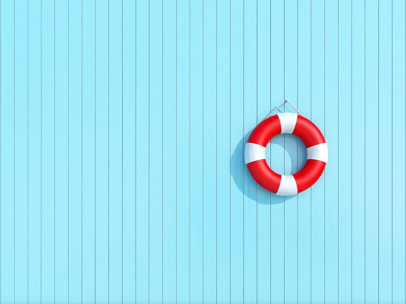 Red lifebuoy hanging up on light blue wooden planks.