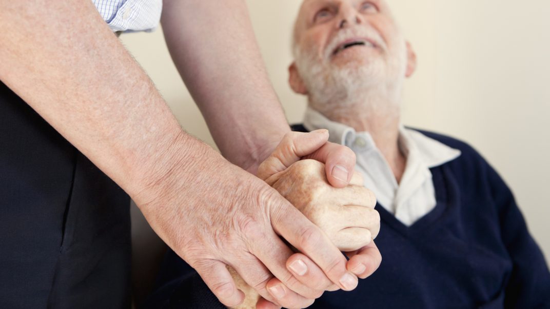 Elderly man looking up at the person he is holding hands with.