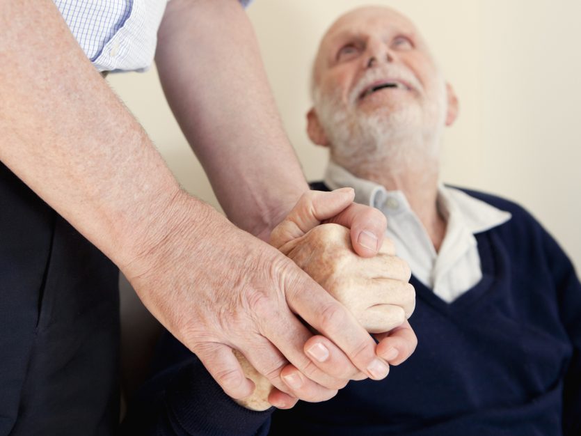 Elderly man looking up at the person he is holding hands with.