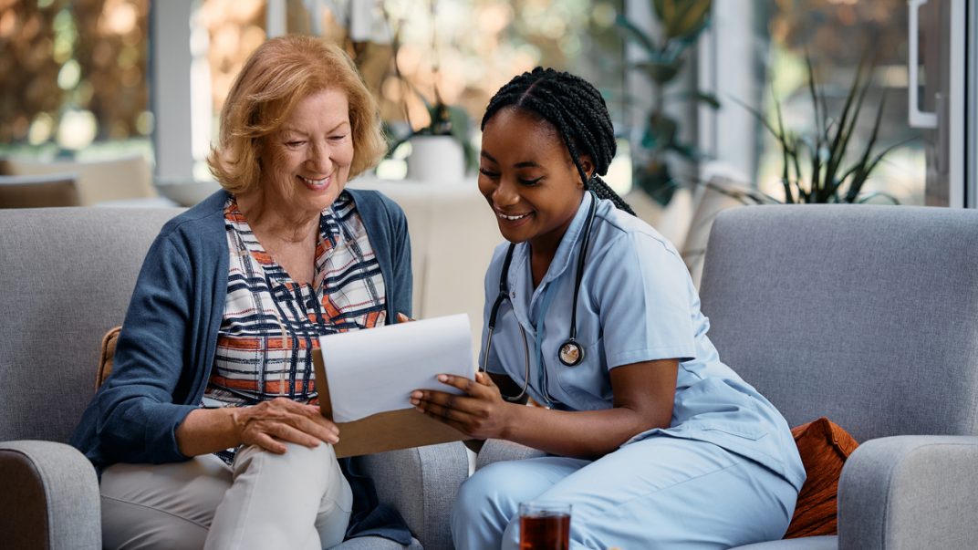 Older adult and a nurse sitting in an office and looking over documents in a clipboard together.