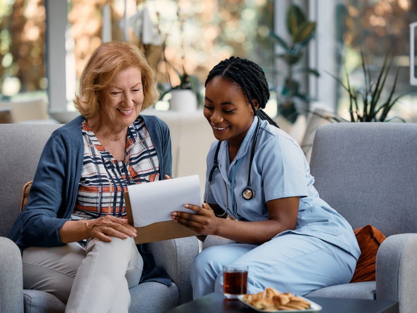 Older adult and a nurse sitting in an office and looking over documents in a clipboard together.