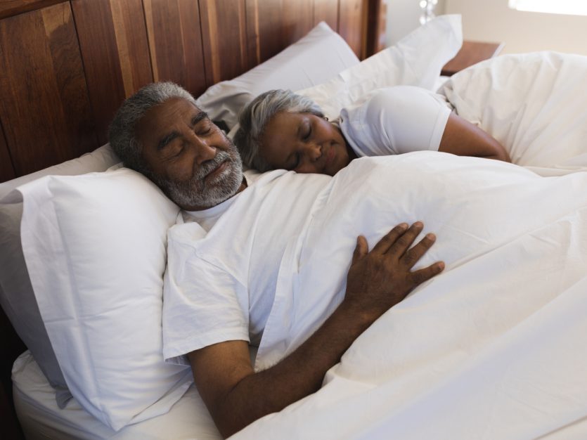 Older adult female and male sleeping in bed.