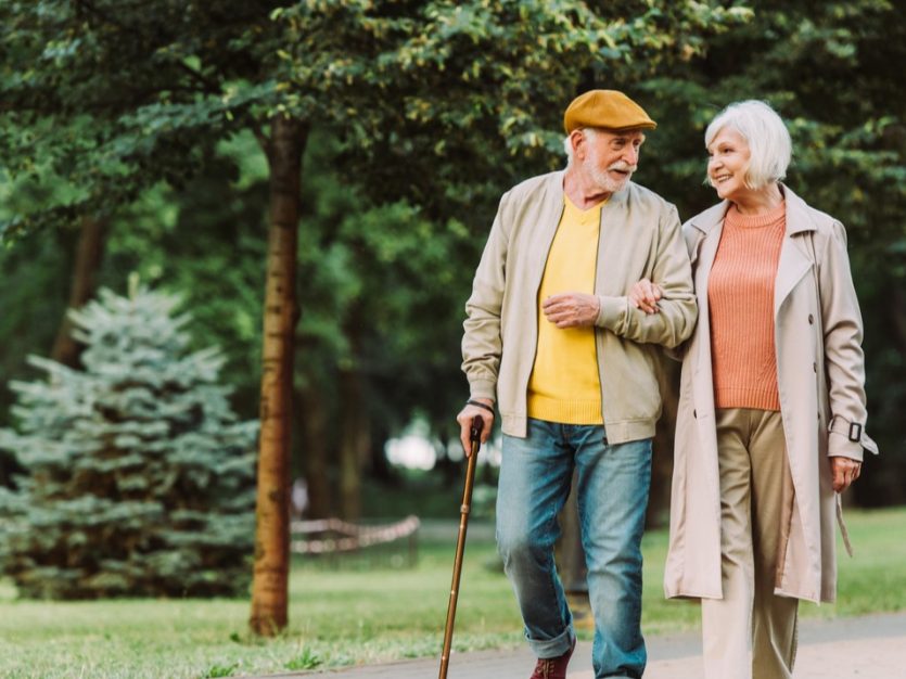 Elderly man and woman walking through a park linking arms.