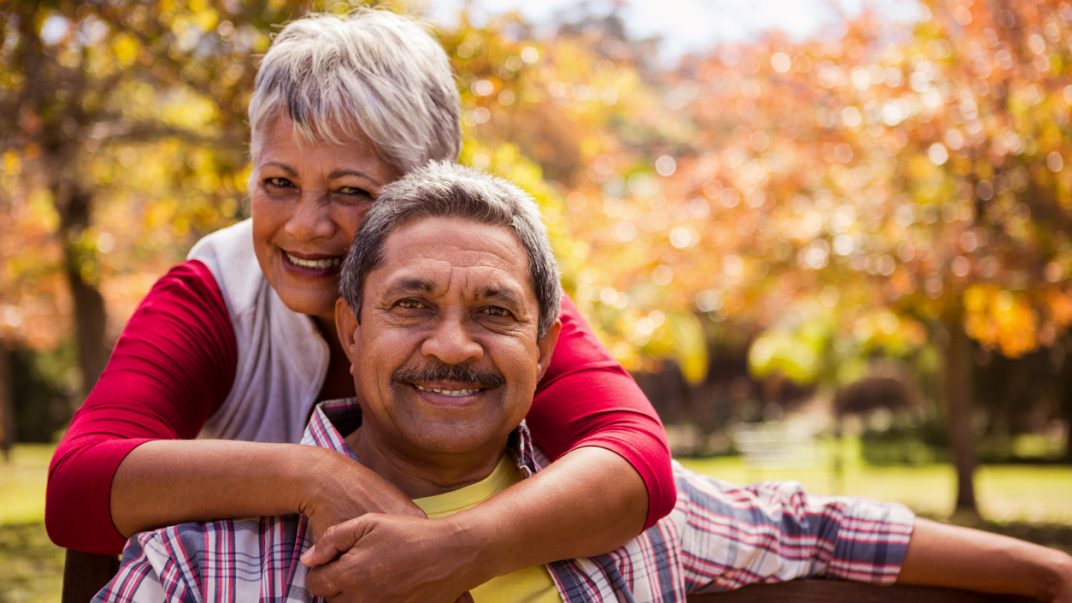 Preventing type 2 diabetes with the “sunshine” vitamin? 1 Older adult male sitting on a park bench on a sunny day, while his wife stands behind the bench and hugs him.