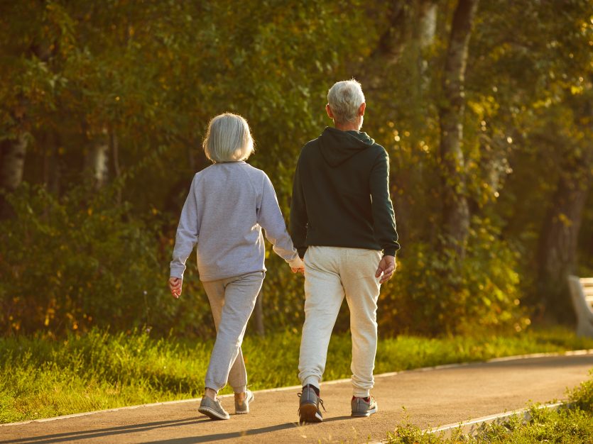 Married Senior Couple Walking Together On A Sunny Summer Evening.