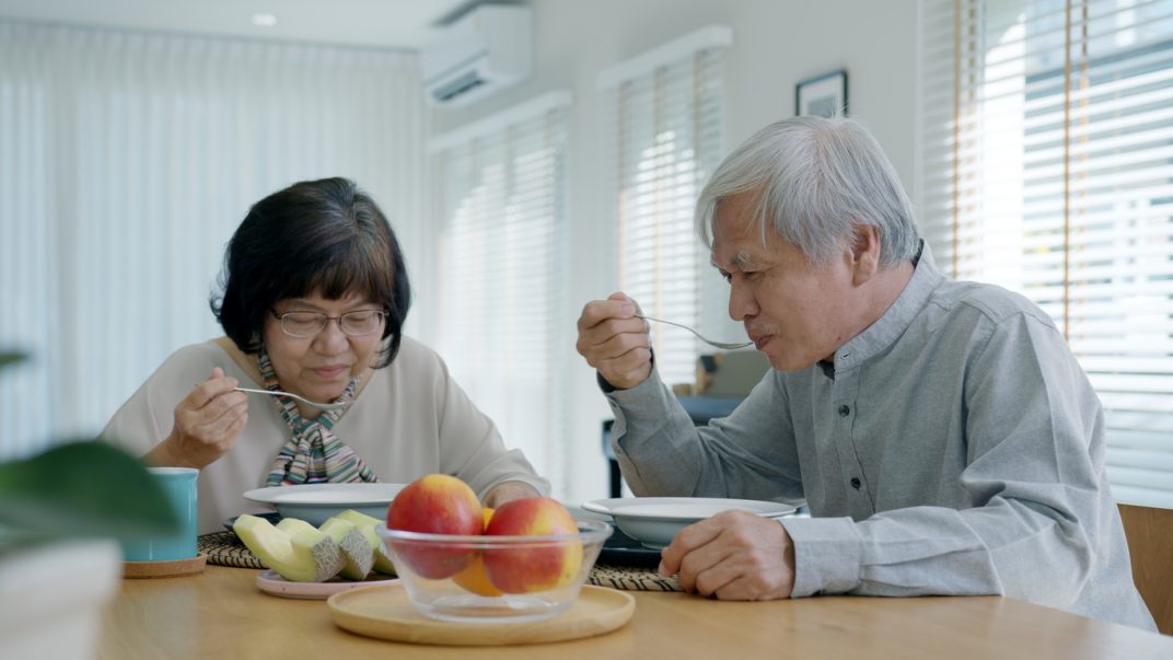 Older adult couple sitting at their dining room table and eating soup.