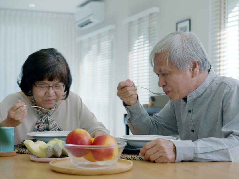 Older adult couple sitting at their dining room table and eating soup.