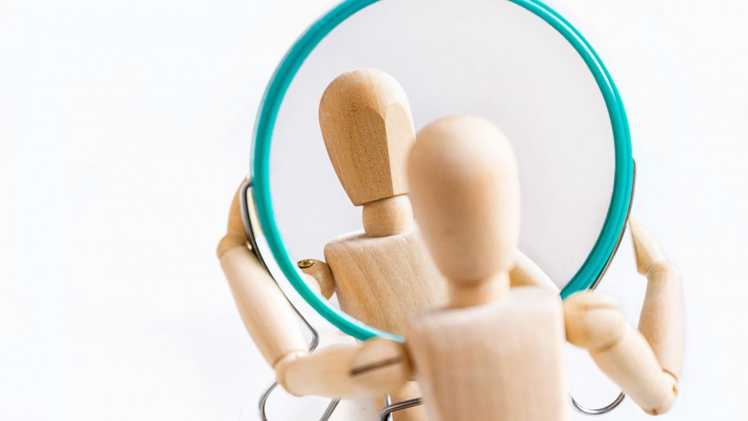 a wooden figurine holding a round mirror