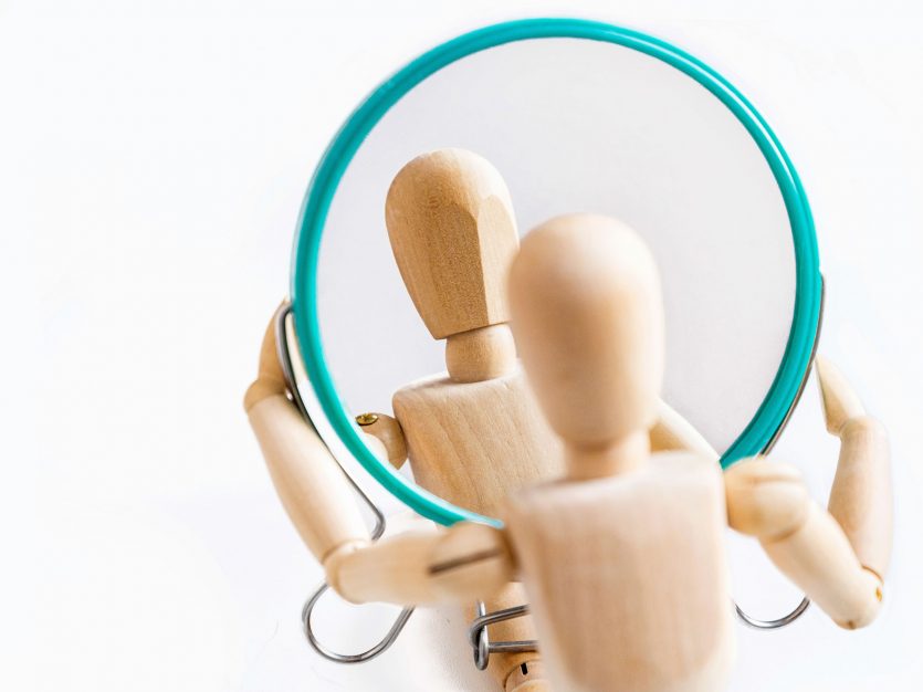 a wooden figurine holding a round mirror