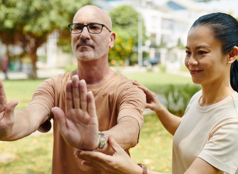 Man doing tai chi in a park with guidance from a teacher.