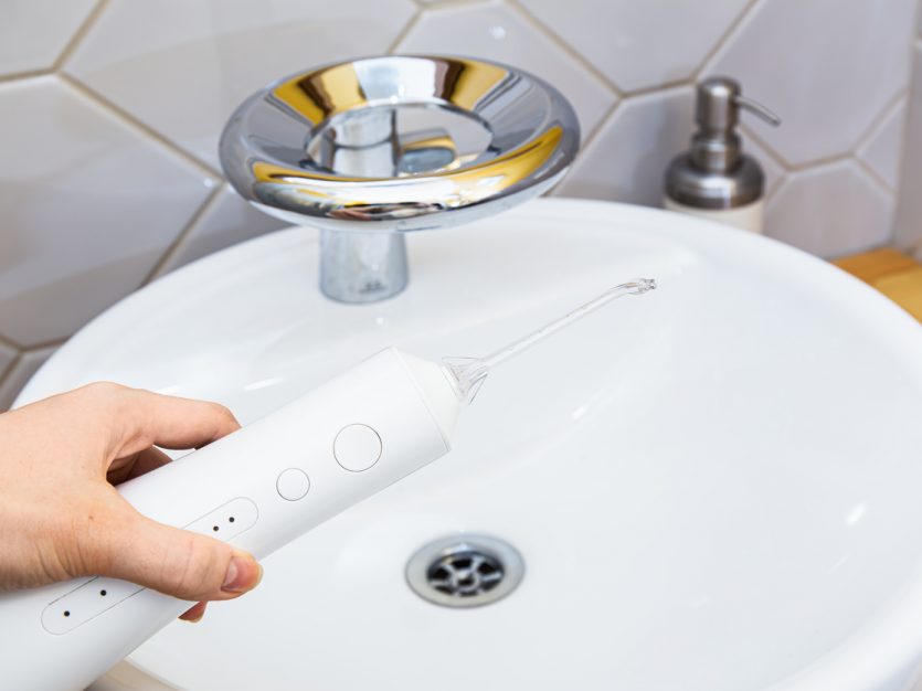 A hand holding a water flosser over a sink in the bathroom.